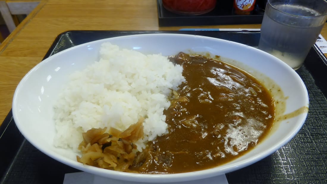 Chicken curry with rice on a canteen tray under dim indoor light — before
