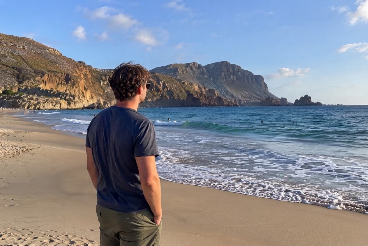 A man looking at the sea on a beach full of tourists — after
