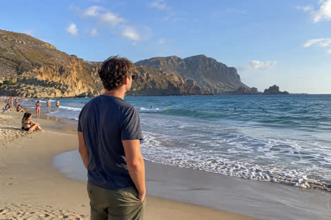 A man looking at the sea on a beach full of tourists